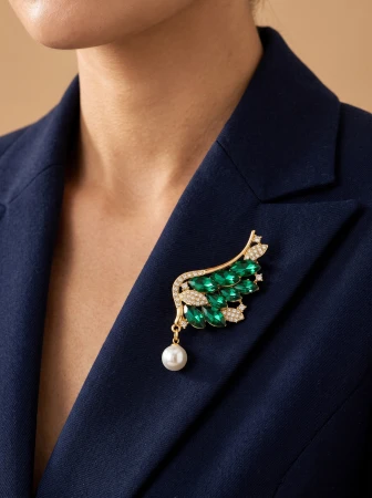 Elegancka broszka w kolorze złota z zielonymi kamieniami i perłową zawieszką